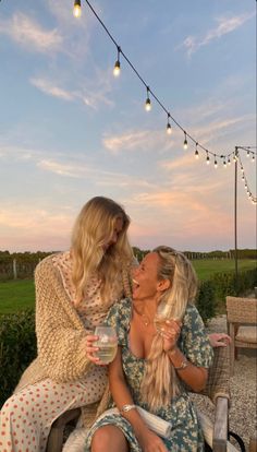 two women sitting on a bench sharing a glass of wine and laughing at each other