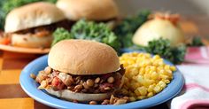 two sandwiches on buns with beans, corn and broccoli in the background