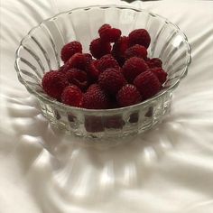 a glass bowl filled with raspberries on top of a white bed sheet,