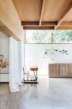 a living room with large windows and wooden furniture in the center, along with a white drapeed wall