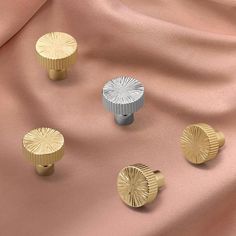 three gold and silver knobs sitting on top of a pink satin surface with two different colors