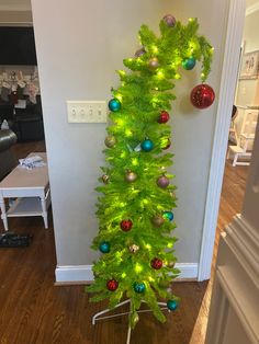 a green christmas tree with ornaments on it in a living room next to a wall