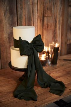 a three tiered white cake with black ribbon on top and candles in the background