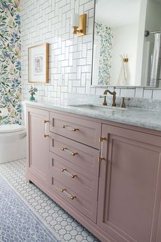 a bathroom with pink cabinets and marble counter tops, gold faucets, and floral wallpaper