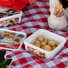 a woman sitting on a picnic blanket holding a doughnut in front of two boxes of donuts