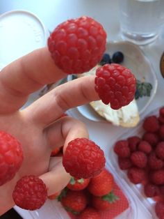 a person holding raspberries in front of some other fruit on the counter top