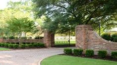 a driveway with a brick fence and stone pillars in the center, surrounded by green grass