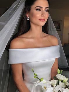 a woman in a white wedding dress holding a bouquet of flowers and wearing a veil