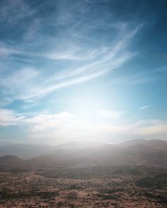 an airplane flying in the sky over a desert area with mountains and clouds behind it