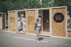 people are walking by some wooden booths on the side of the road with signs in them