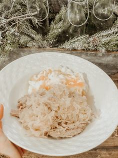 someone holding a white plate with rice and meat on it in front of a christmas tree