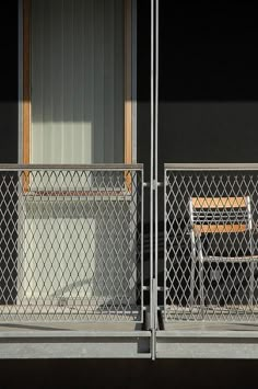 two wooden chairs sitting on top of a metal fence next to a building with windows