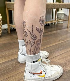 a woman's legs with tattoos on them and flowers painted on the bottom of her leg