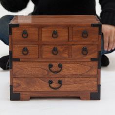 a person sitting on the floor next to a wooden dresser with black handles and knobs