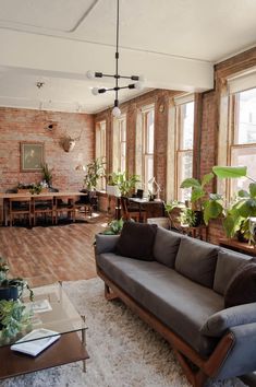 a living room filled with lots of furniture and plants on top of a hard wood floor