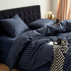 a bed with blue and white striped comforter next to a black headboard on a wooden floor