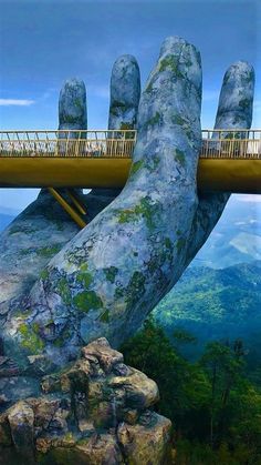 a giant hand with a bridge over it in the middle of a mountain range, surrounded by trees and mountains