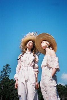 two women in white dresses and straw hats standing next to each other on a sunny day