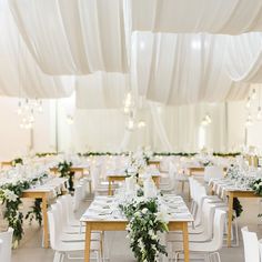 tables and chairs are set up with white linens, greenery, and chandeliers