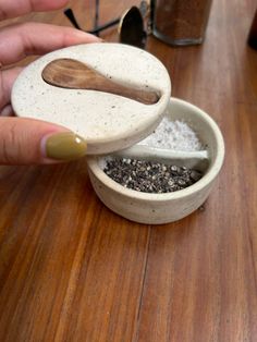 a person holding a wooden spoon over a bowl filled with sea salt and oregano