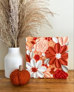 an orange and white flowered card next to a vase with dried grass