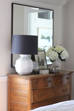 a white vase sitting on top of a wooden dresser next to a black and white lamp