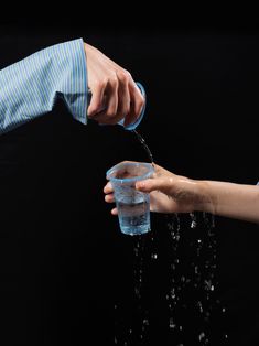 two people are pouring water from a plastic cup into each other's hands, on a black background