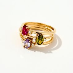 three gold rings with different colored stones on each one, set against a white background