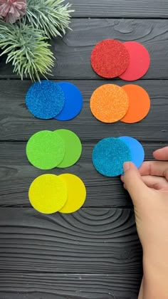 someone is making colorful paper circles out of construction paper on a wooden table next to a potted plant