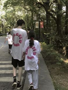 a man and woman walking down a sidewalk in the park with trees on both sides