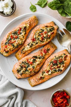 three salmon fillets on a white plate with tomatoes and spinach next to it