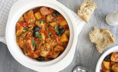 a white bowl filled with stew next to two slices of bread on top of a table