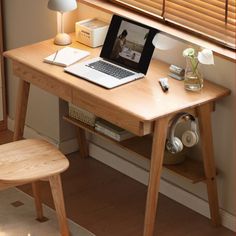 an open laptop computer sitting on top of a wooden desk next to a lamp and window