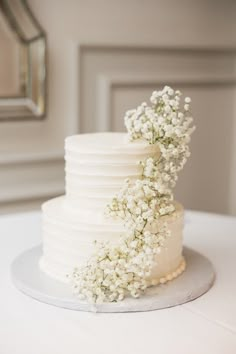 a white wedding cake with flowers on top is sitting on a table in front of a mirror