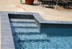 an empty swimming pool with chairs and tables in the back ground, next to it