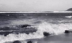 black and white photograph of waves crashing on the beach with an island in the distance