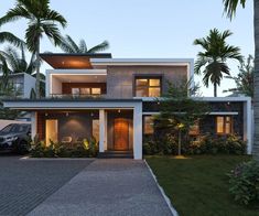 a modern house with palm trees in the front yard and driveway leading up to it