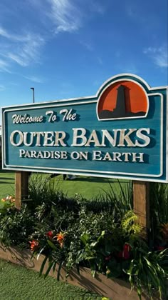 welcome to the outer banks paradise on earth sign in front of green grass and flowers