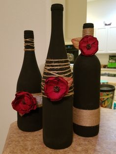 three wine bottles decorated with red flowers and twine on a counter in a kitchen