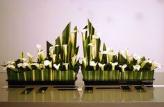 two vases with white flowers are sitting on a glass table in front of a wall