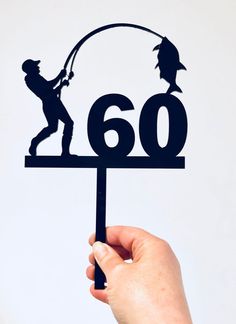 a hand holding up a black metal sign with the number 60 and a silhouette of a man fishing