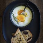 a black plate topped with bread and eggs next to a bowl of yogurt