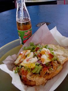 a chicken sandwich with lettuce, tomato and cheese on it next to a bottle of soda