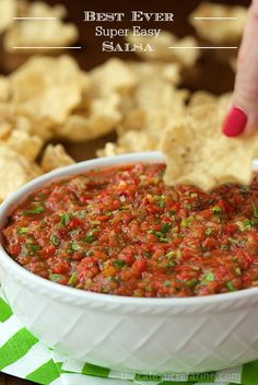 a person dipping salsa into a white bowl with tortilla chips on the side