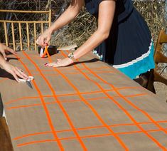 two women sanding on top of an outdoor table with orange lines painted on it