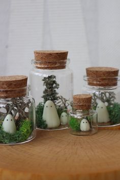 three glass jars filled with moss and fake white ghost figurines sitting on top of a wooden table