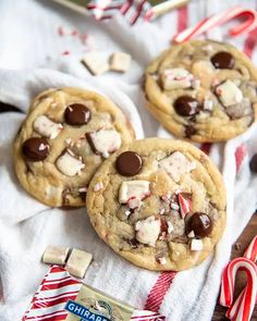 three chocolate chip cookies sitting on top of a white towel next to candy canes