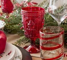 the table is set for christmas dinner with red decorations and glassware, including an apple