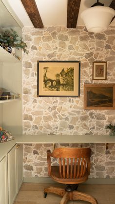 a wooden chair sitting in front of a stone wall next to a shelf with pictures on it