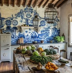 a kitchen with blue and white tiles on the wall, wooden table surrounded by vegetables